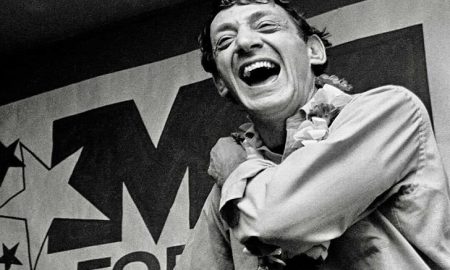 Quotes from Harvey Milk - Laughing joyfully in front of a "VOTE" campaign poster in a black and white photo.